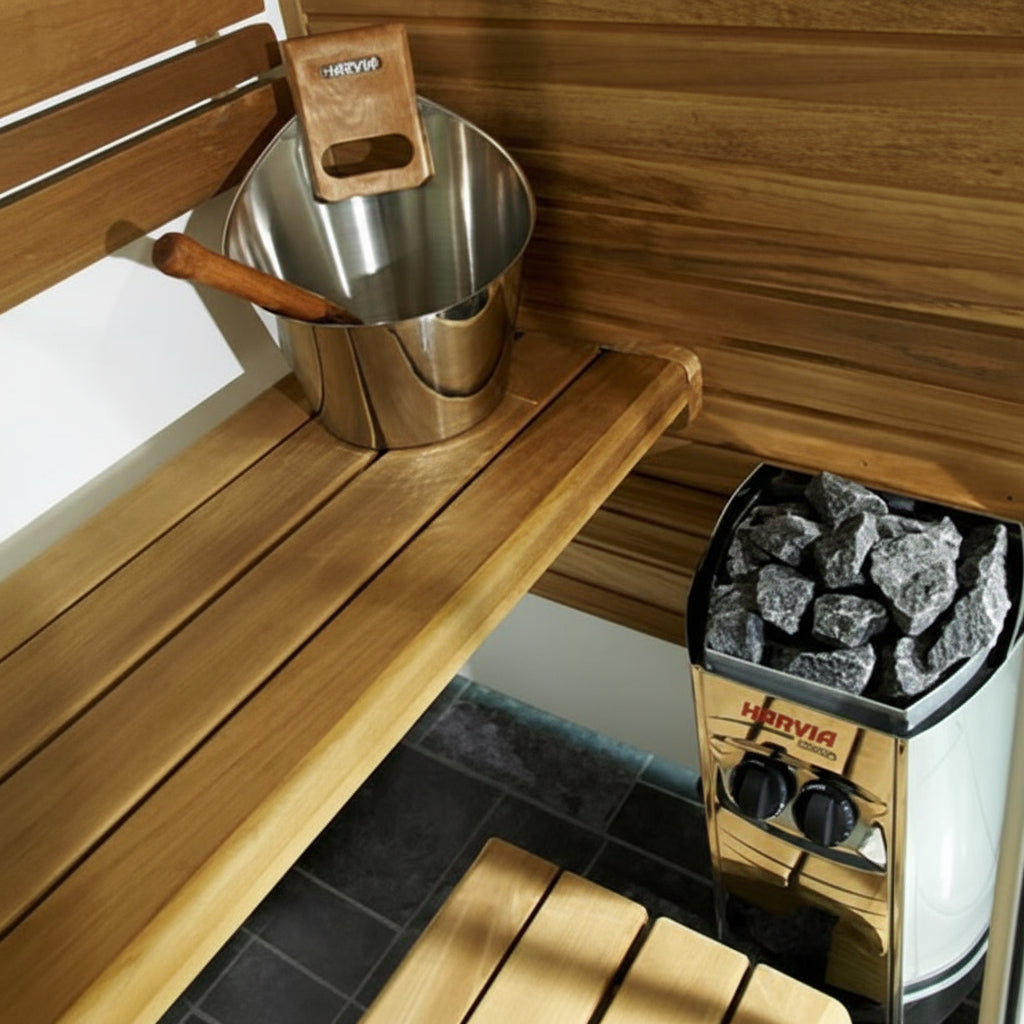 The image shows a compact electric sauna heater, the Harvia Vega 3500, installed in a sauna. The heater is wall-mounted, with sauna stones on top, and is surrounded by wooden sauna benches.