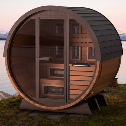 Wooden barrel-shaped sauna by a lake with mountains in the background