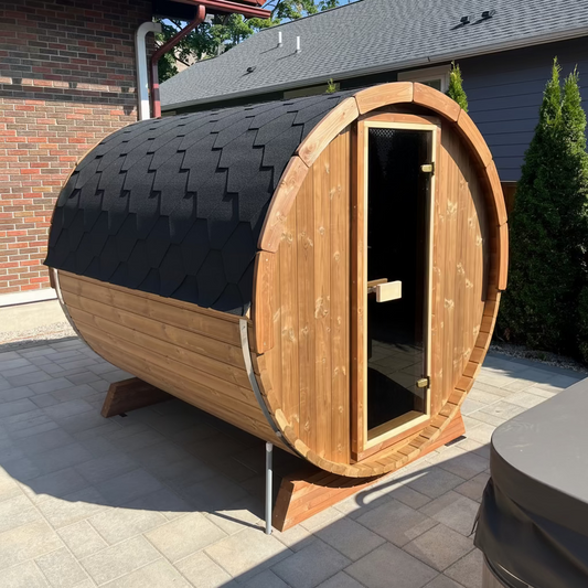 A six person barrel sauna made from thermo-spruce, with a black shingle roof, a bronze glass door, and stainless steel barrel bands.