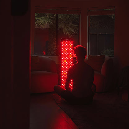 Person sitting in a dark room with a red lighted object in the background